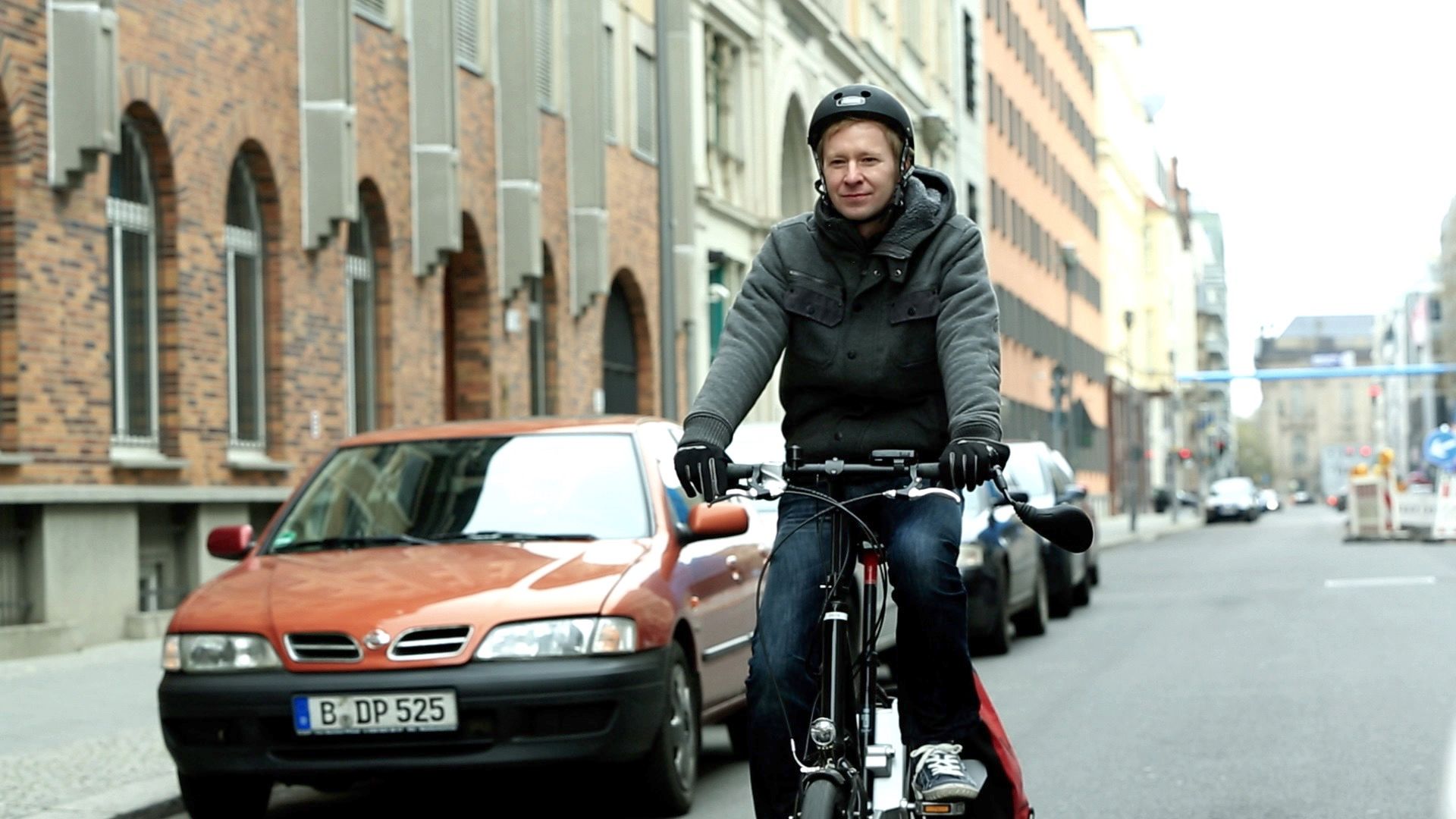 Radfahrer mit Helm fährt durch eine Straße vorbei an einem geparkten Auto