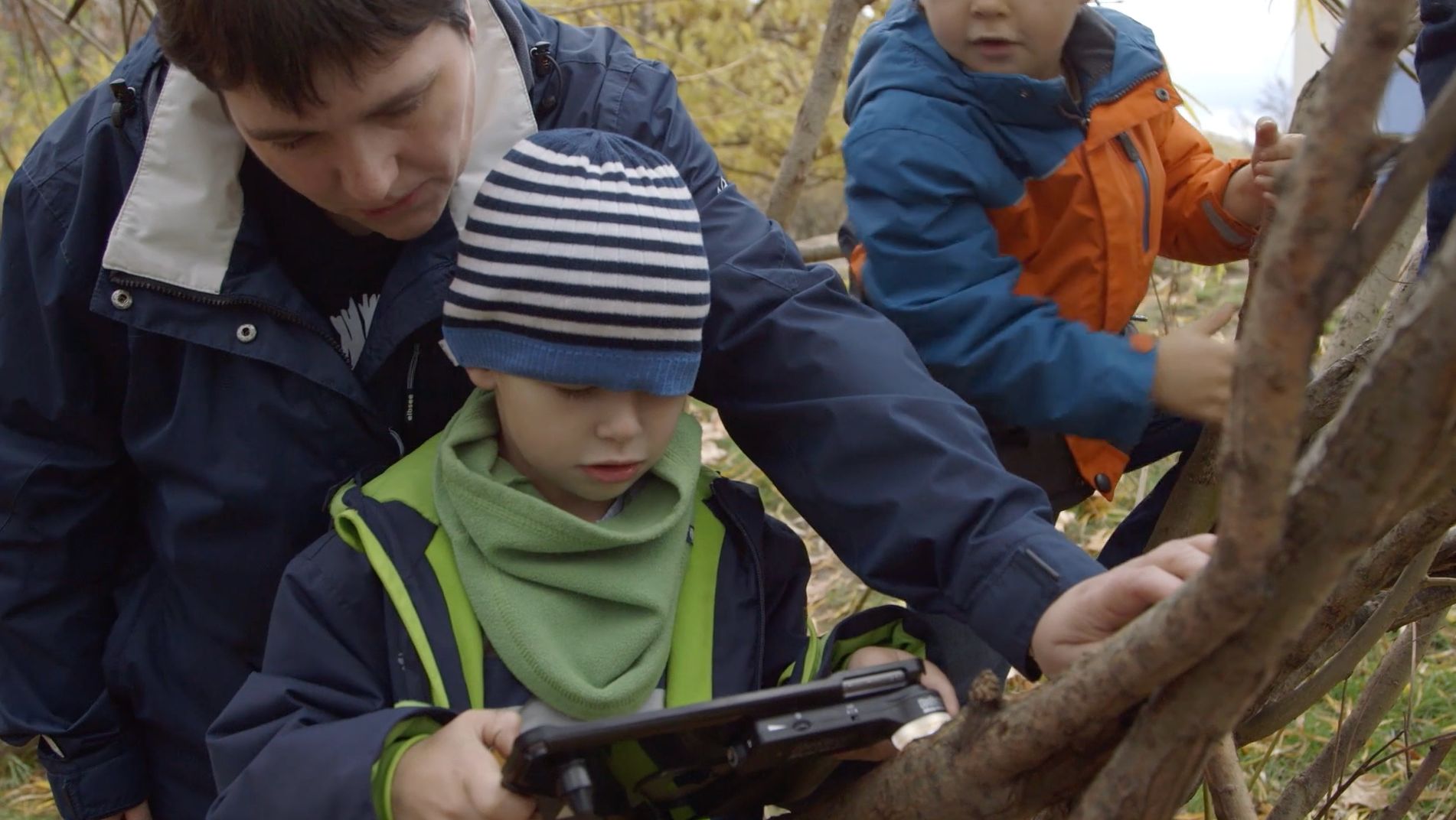 Erwachsener und Kinder in Winterkleidung untersuchen im Wald etwas auf einem Tablet