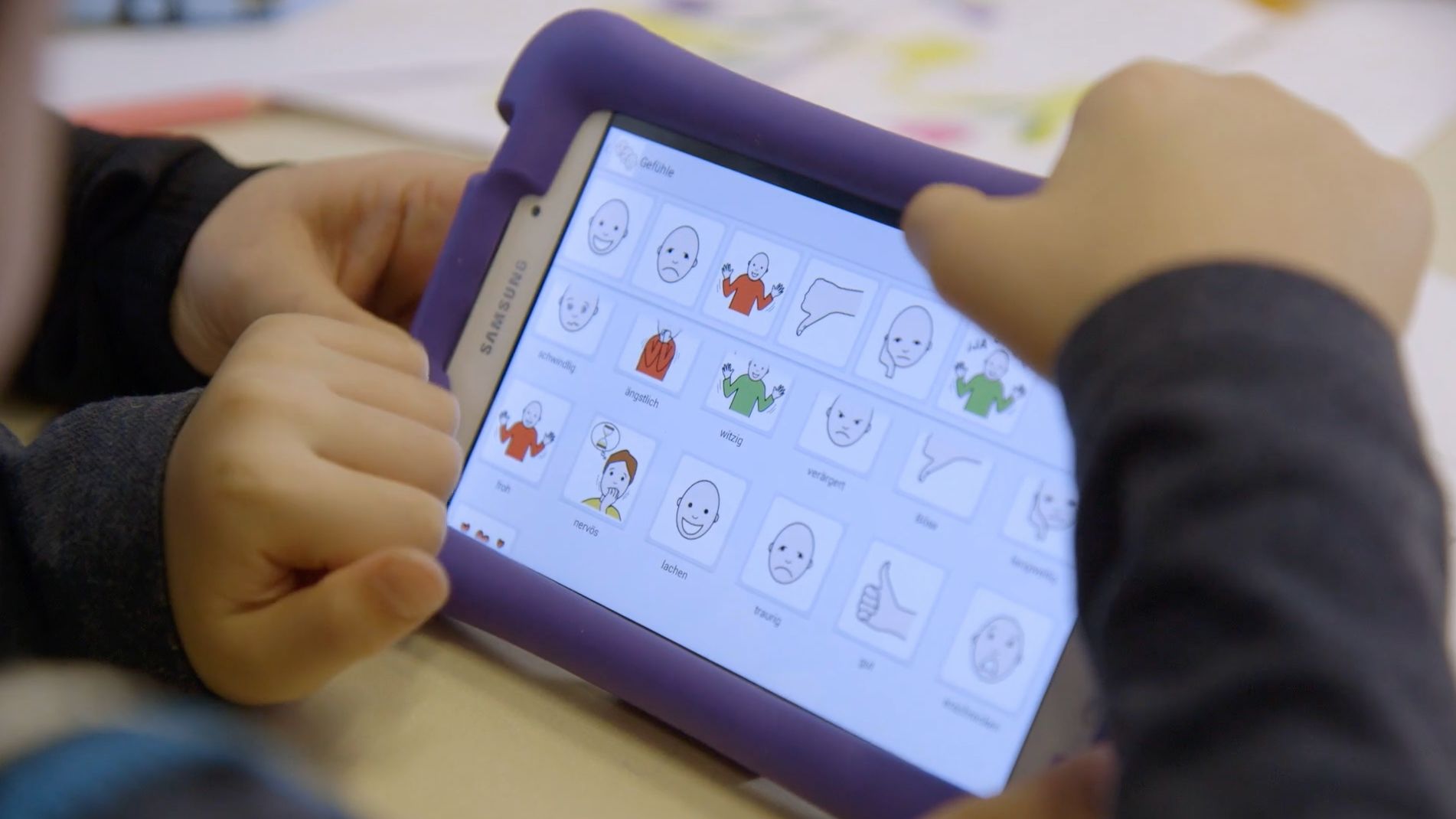 Kinderhände halten ein Tablet mit einer Gefühle-App, Bildkarten zeigen froh, traurig und wütend