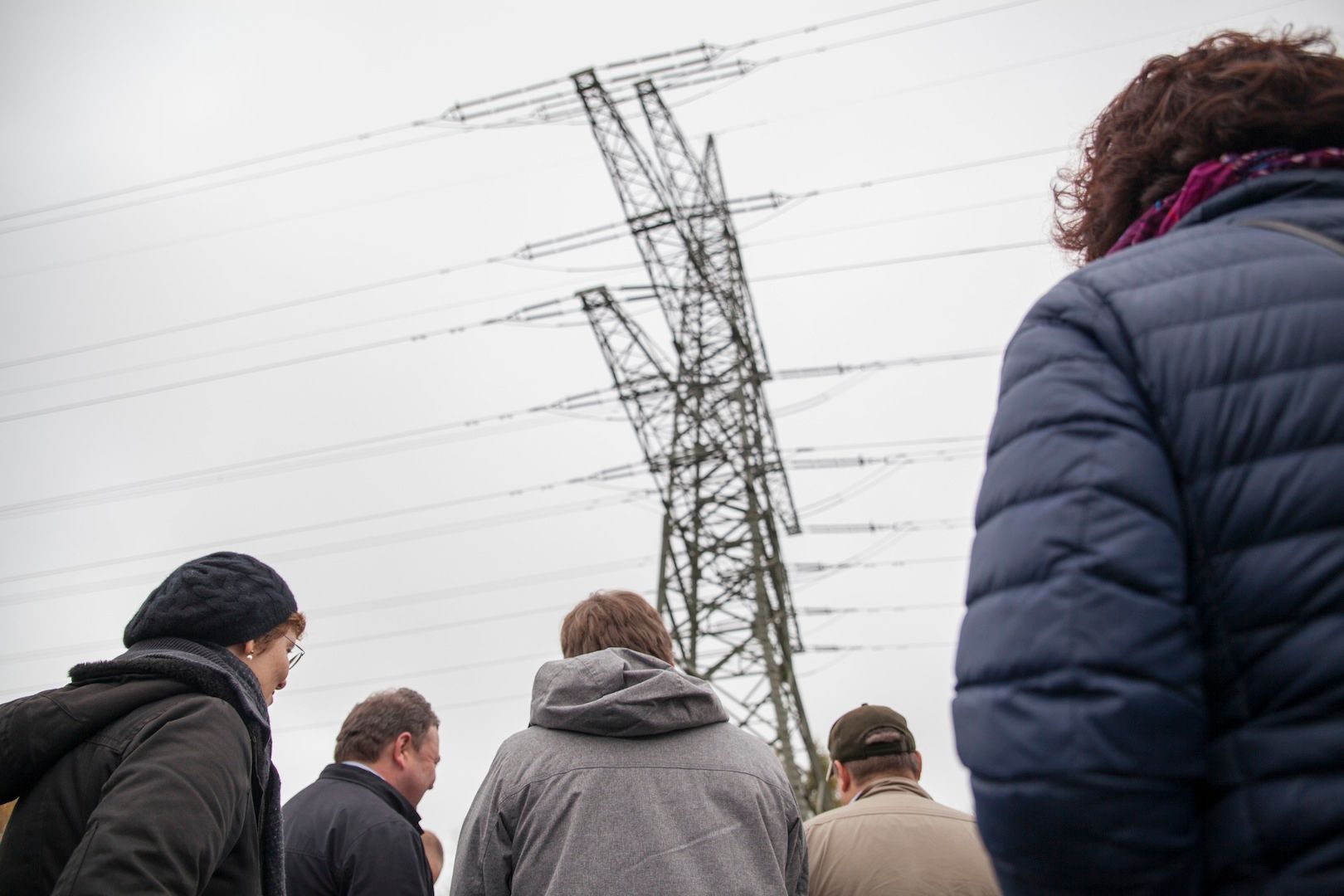 Gruppe blickt von unten zu einem hohen Strommast vor bewölktem Himmel empor