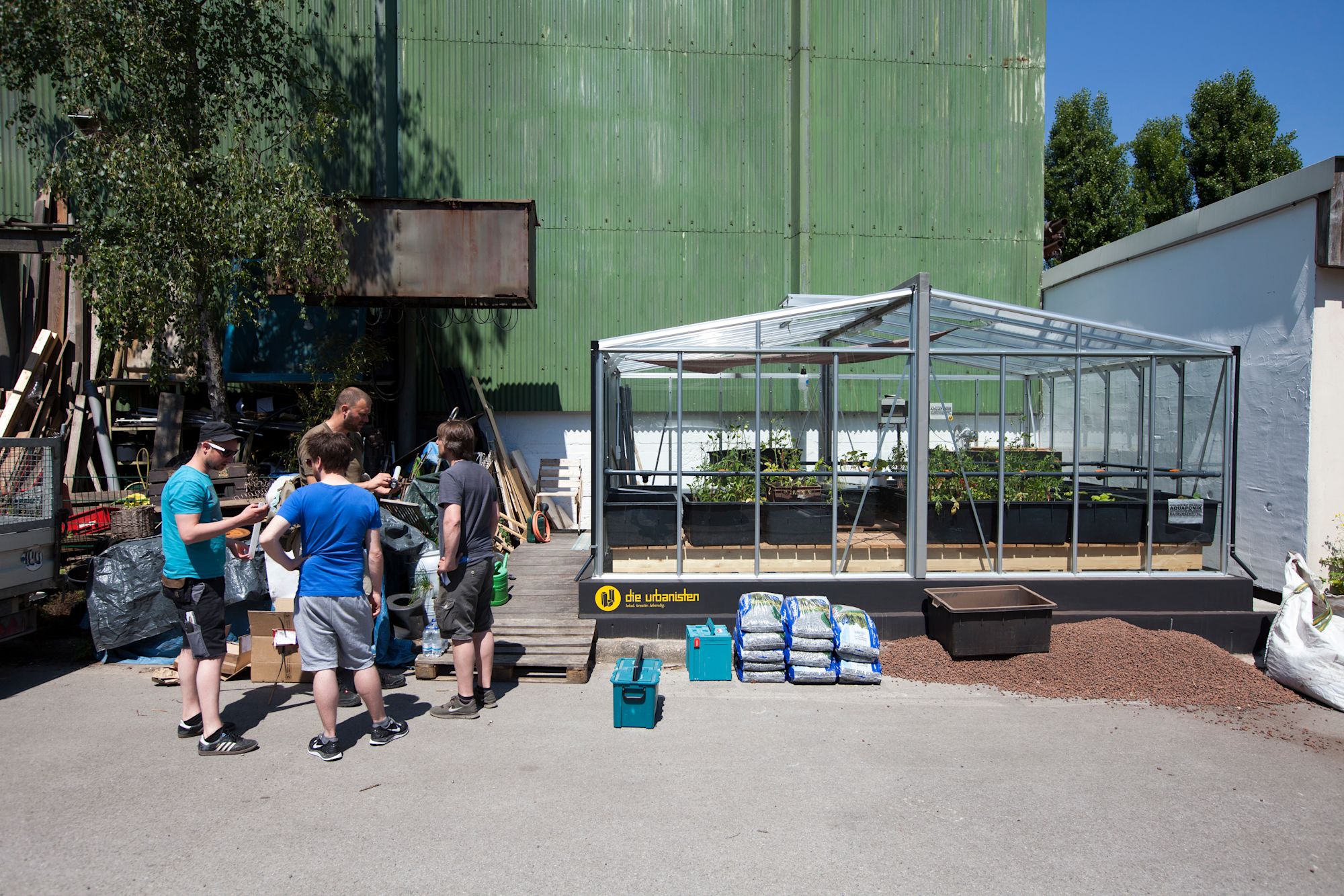 Mehrere Personen begutachten ein Gewächshaus mit Aquaponik-Anlage vor einer Lagerhalle