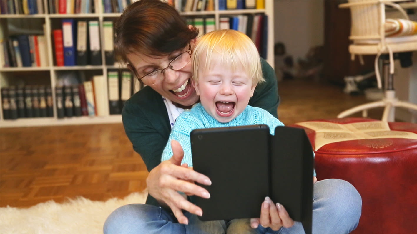 Frau lacht mit einem johlenden Kleinkind, das ein Tablet in den Händen hält