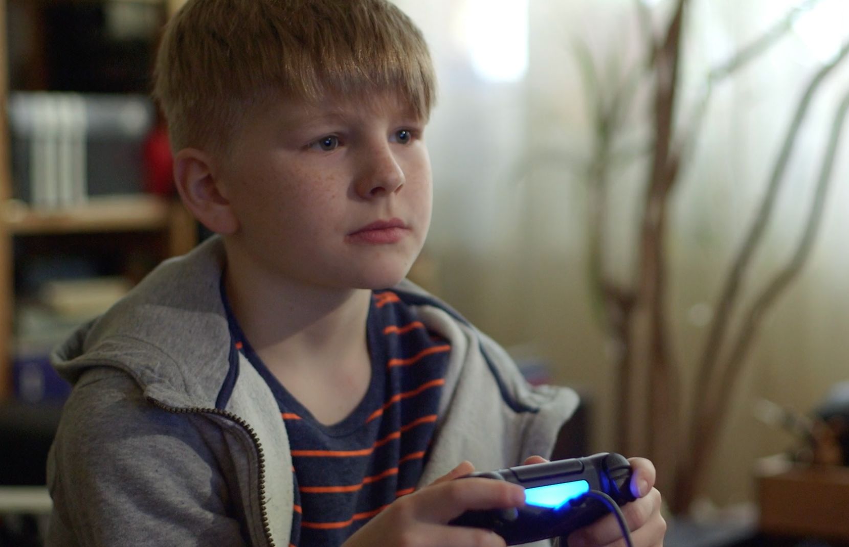 Aufmerksamer Junge in Kapuzenjacke hält einen leuchtenden Spielecontroller