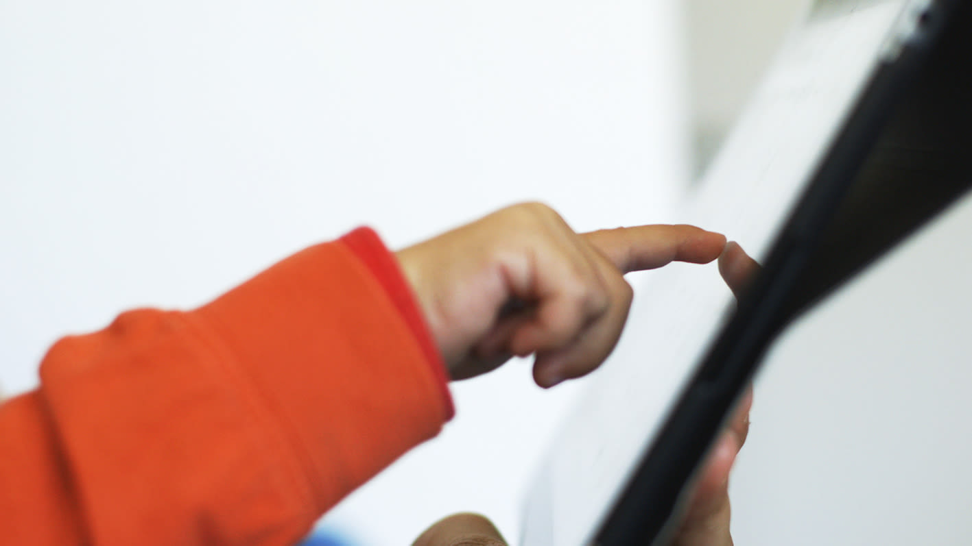 Nahaufnahme eines Kinderfingers, der den Rand eines Tablets berührt