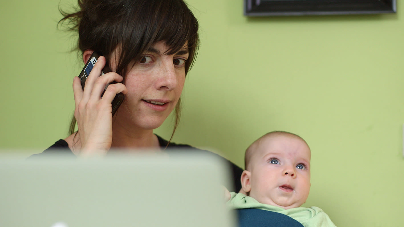 Frau telefoniert mit dem Smartphone, während sie ein Baby auf dem Arm trägt