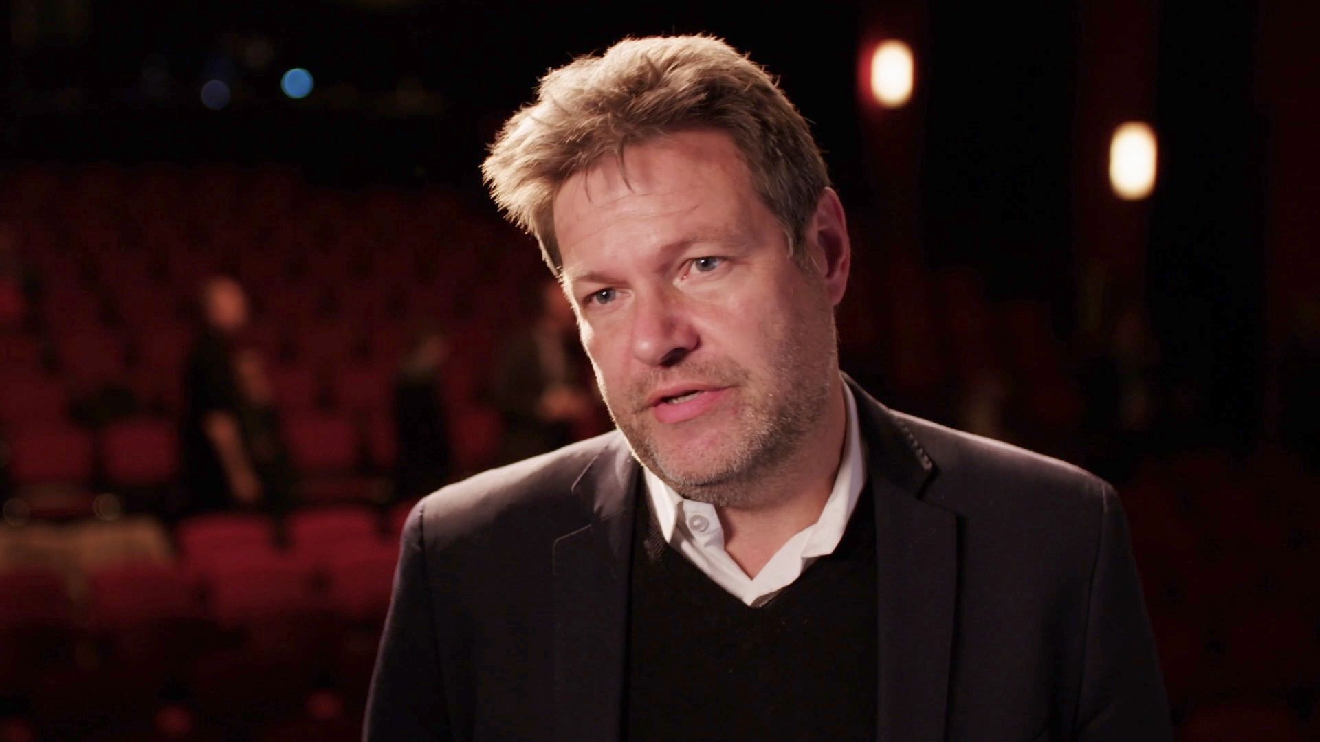 Mann in dunklem Sakko im Interview vor unscharfen roten Theatersitzen