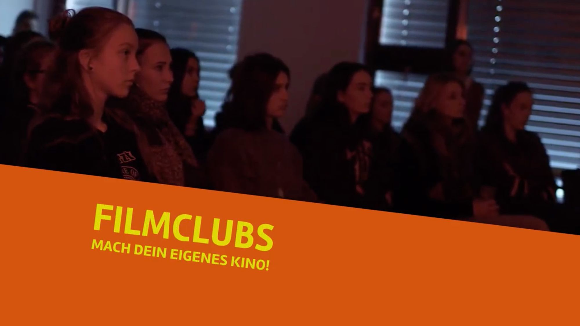 Titelkarte „Filmclubs – Mach dein eigenes Kino!“ vor Zuschauern im abgedunkelten Raum