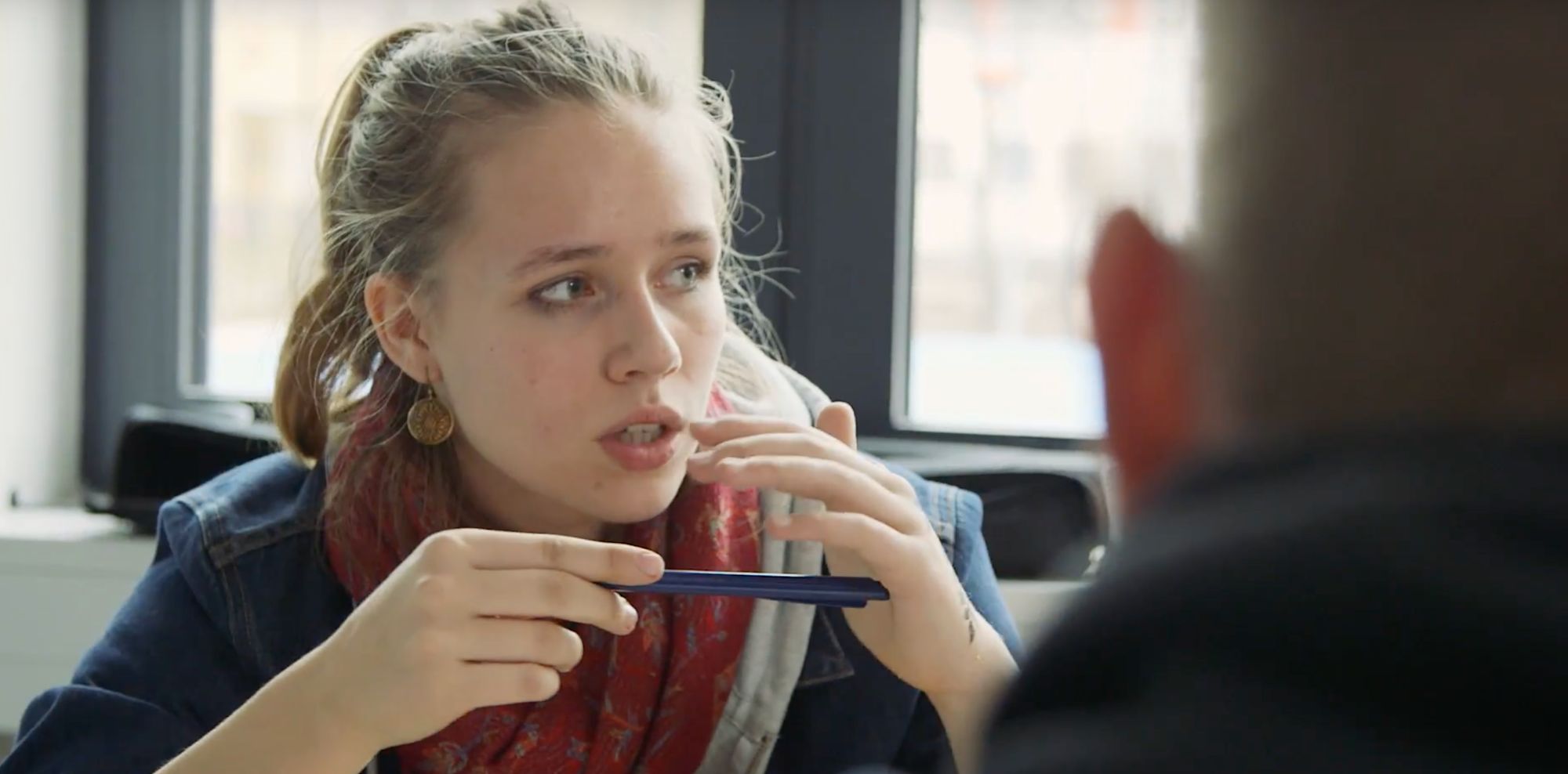 Junge Frau mit buntem Schal spricht gestikulierend und hält ein Smartphone