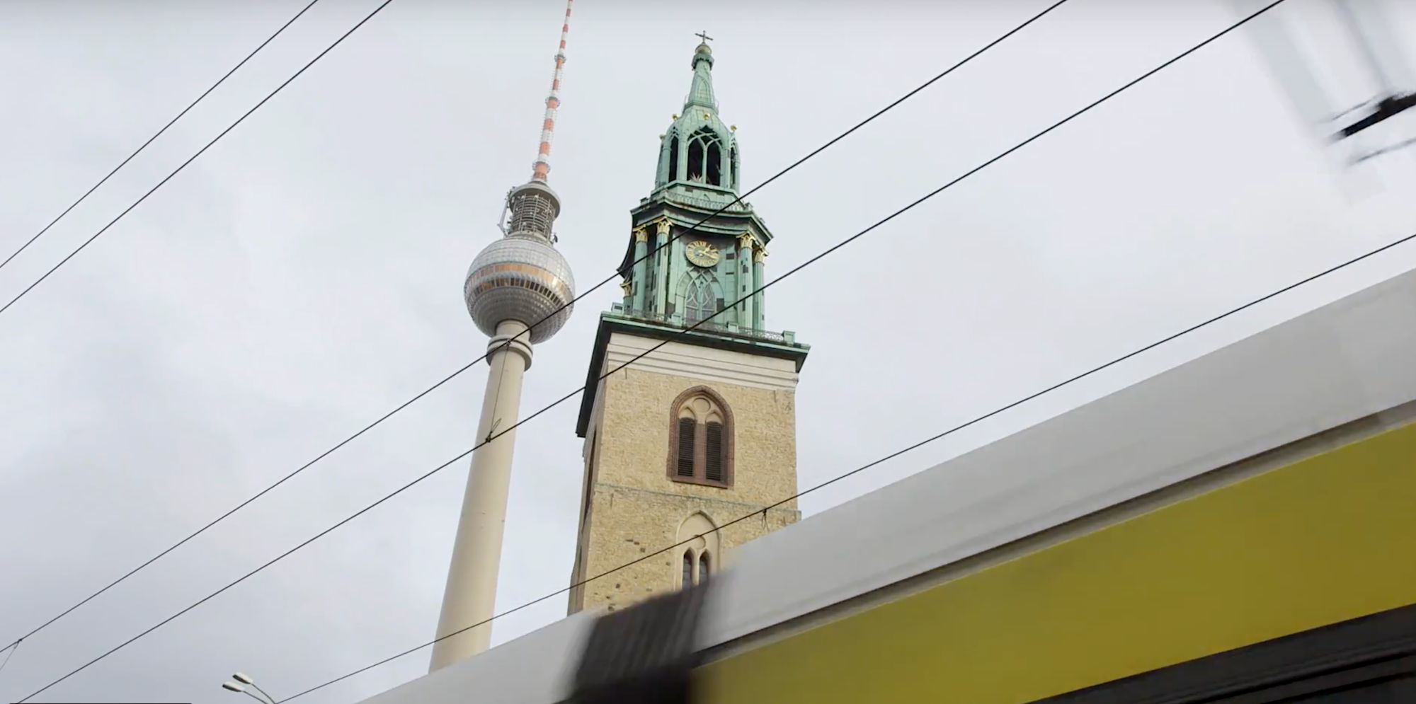 Fernsehturm und Kirchturm der Marienkirche ragen hinter einer vorbeifahrenden Straßenbahn auf