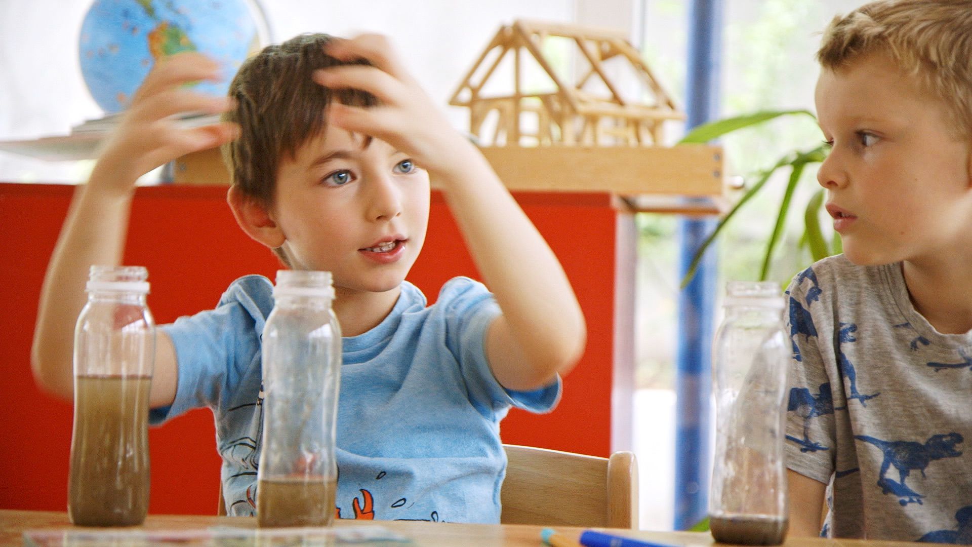 Zwei Jungen sitzen vor trüben Wasserflaschen und diskutieren ihr Experiment