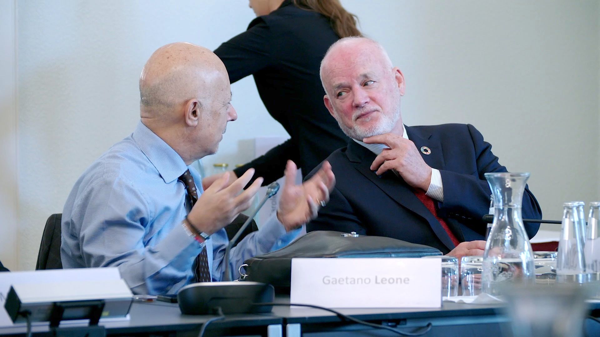 Zwei Männer im Gespräch am Konferenztisch, Namensschild „Gaetano Leone“