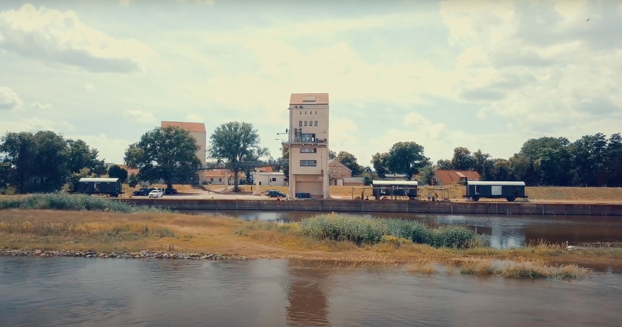 Blick über den Fluss auf einen Aussichtsturm und Bahnwaggons am gegenüberliegenden Ufer