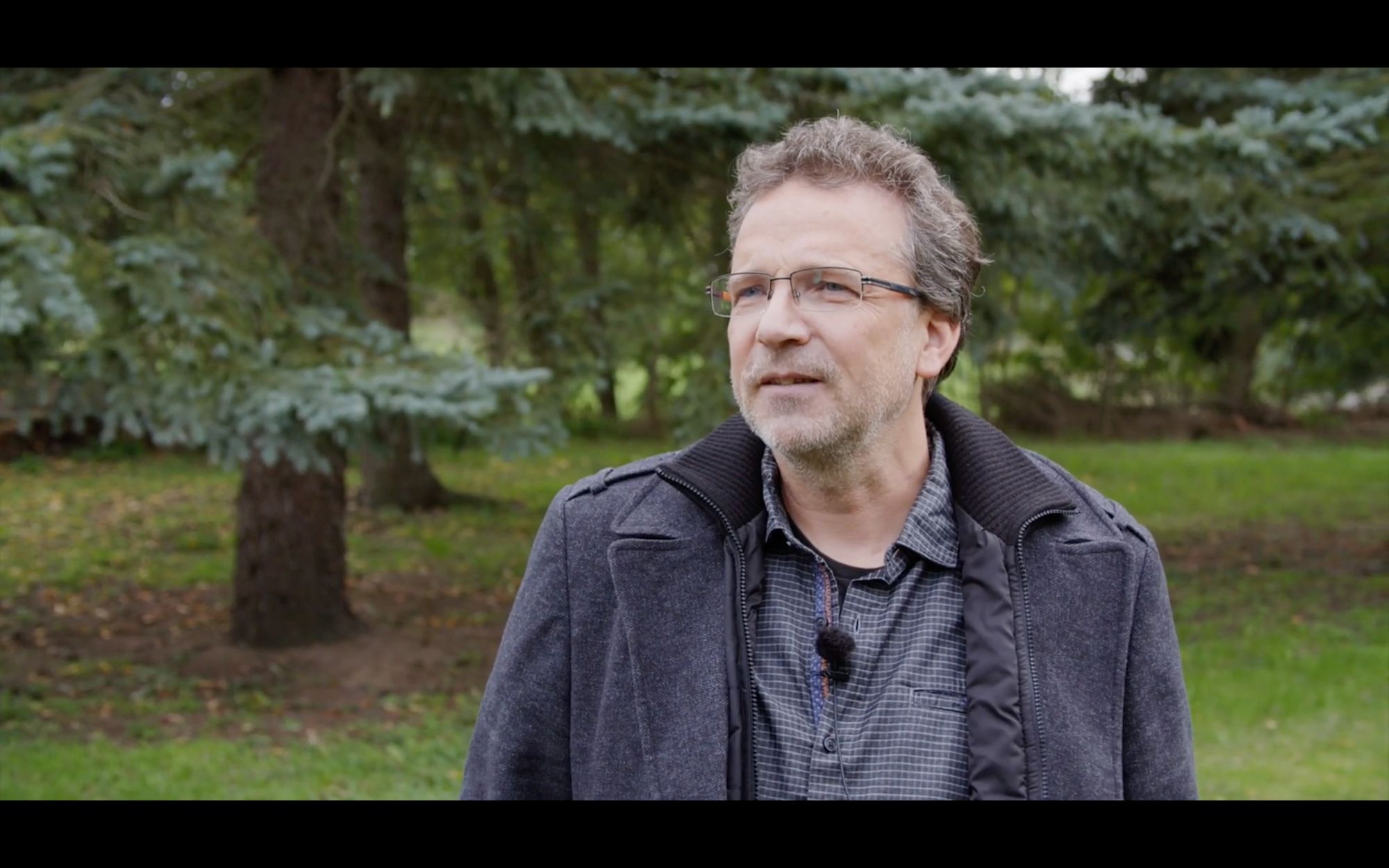Ein Mann mit Brille wird im Freien vor Bäumen interviewt
