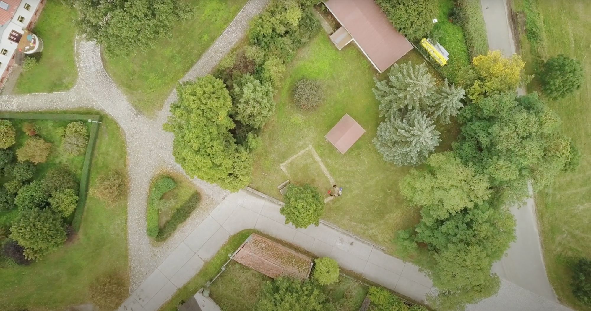 Luftaufnahme eines Kirchgartens mit Wegen, Bäumen und zwei spielenden Kindern