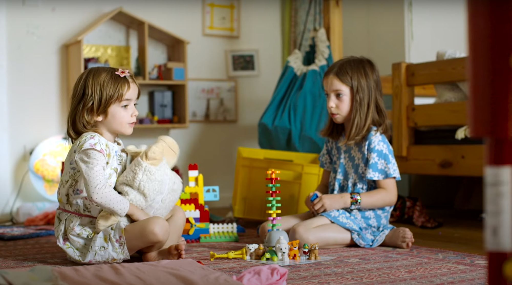 Zwei Mädchen sitzen im Kinderzimmer auf dem Boden und spielen mit Kuscheltier und Bauklötzen