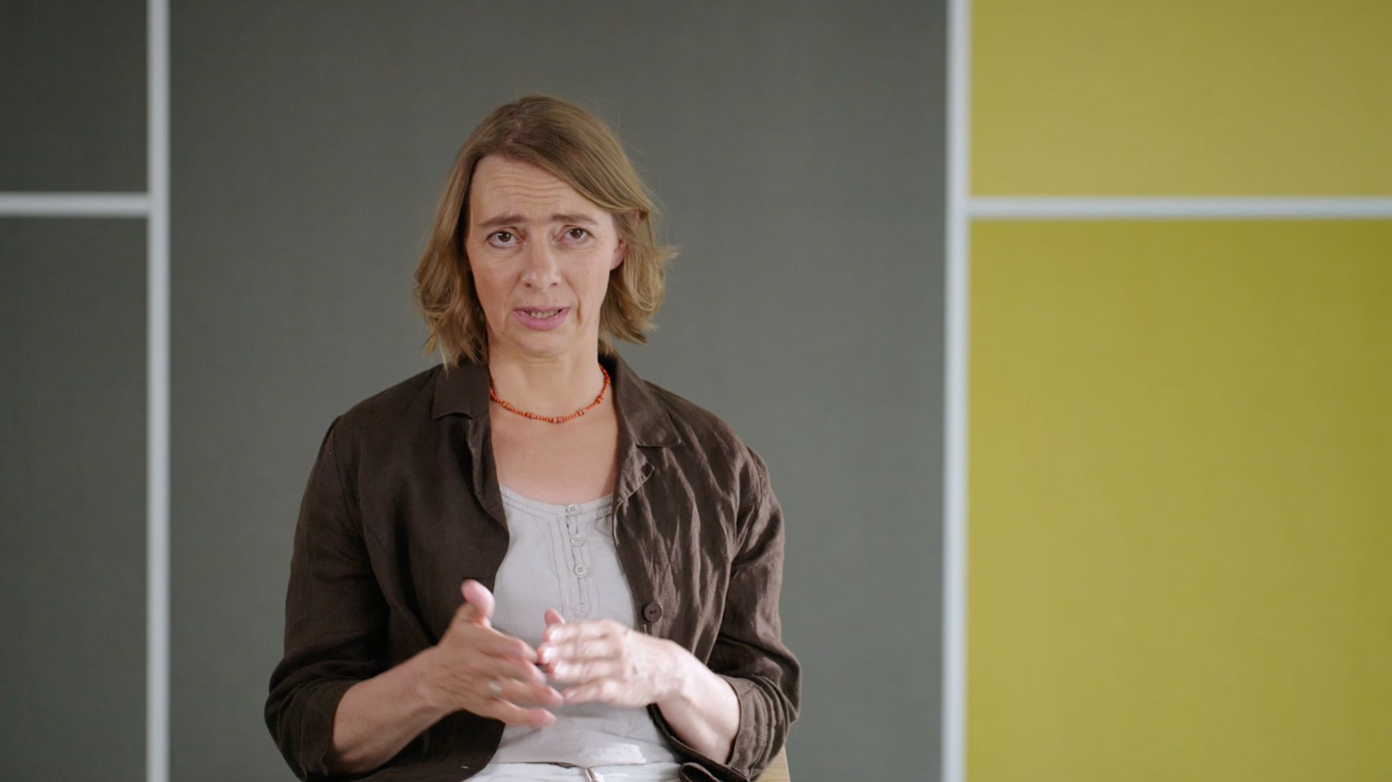 Frau im Interview vor grauer Wand mit ernstem Gesichtsausdruck