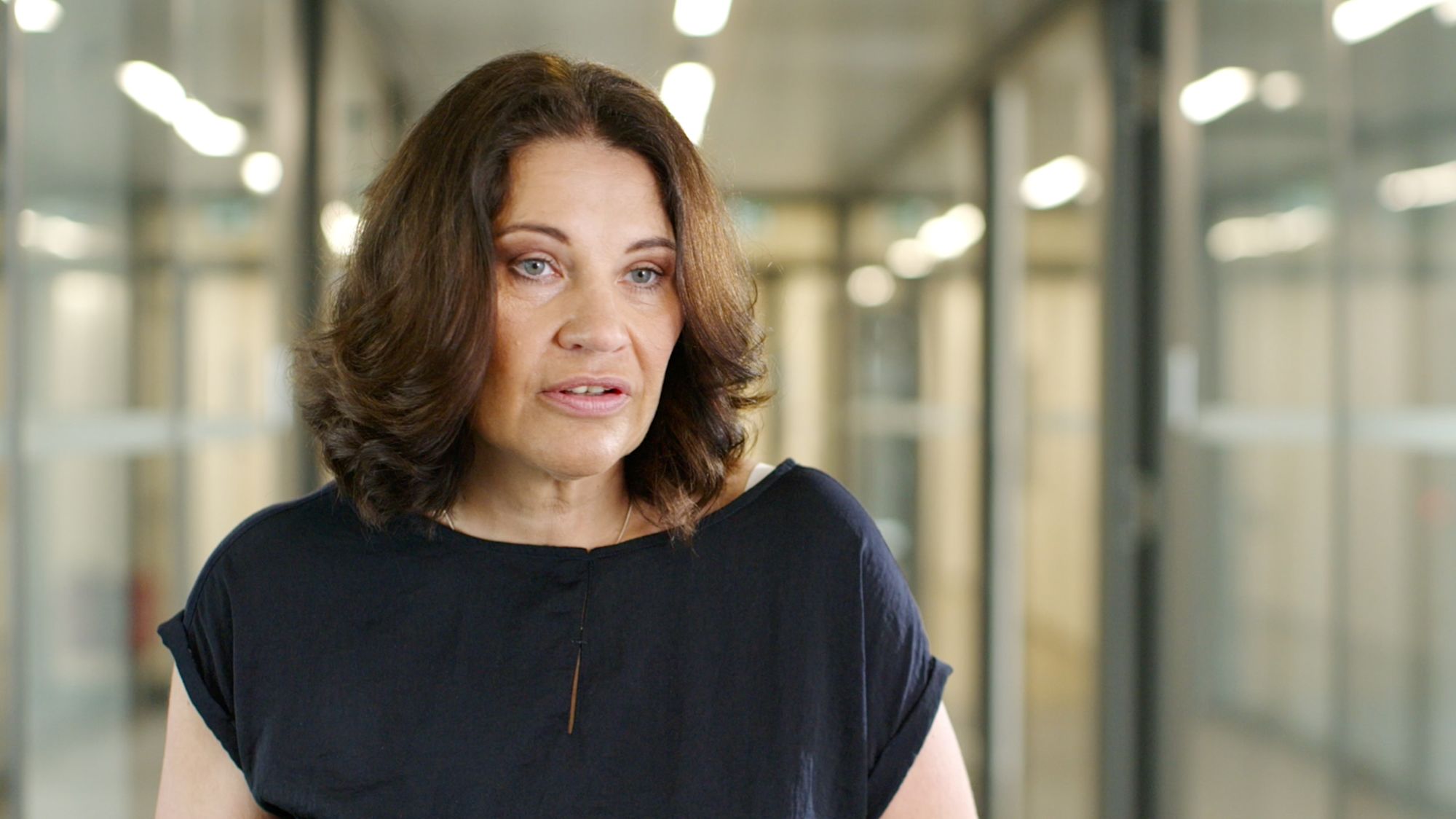 Frau im Interview in einem Flur mit Glastüren vor unscharfem Hintergrund