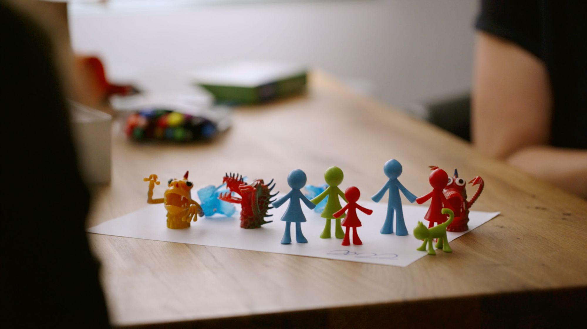 Kleine Spielfiguren von Menschen und Fantasiewesen stehen aufgereiht auf einem Blatt Papier