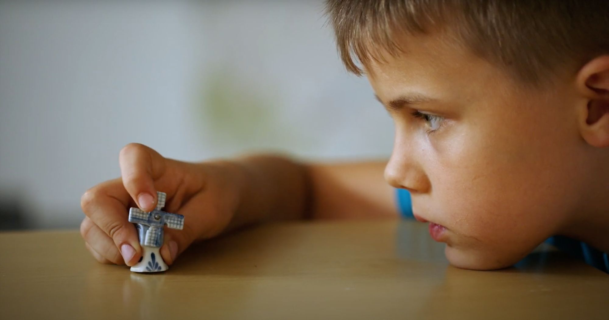 Junge betrachtet aufmerksam eine kleine Windmühle aus Porzellan auf einem Tisch