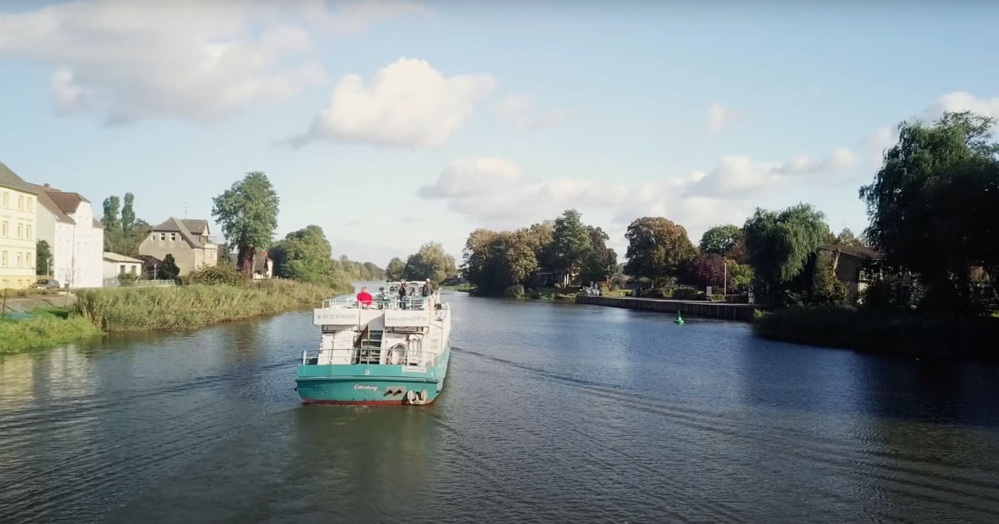 Fahrgastschiff „Oderberg“ auf einem Fluss zwischen Bäumen und Häusern