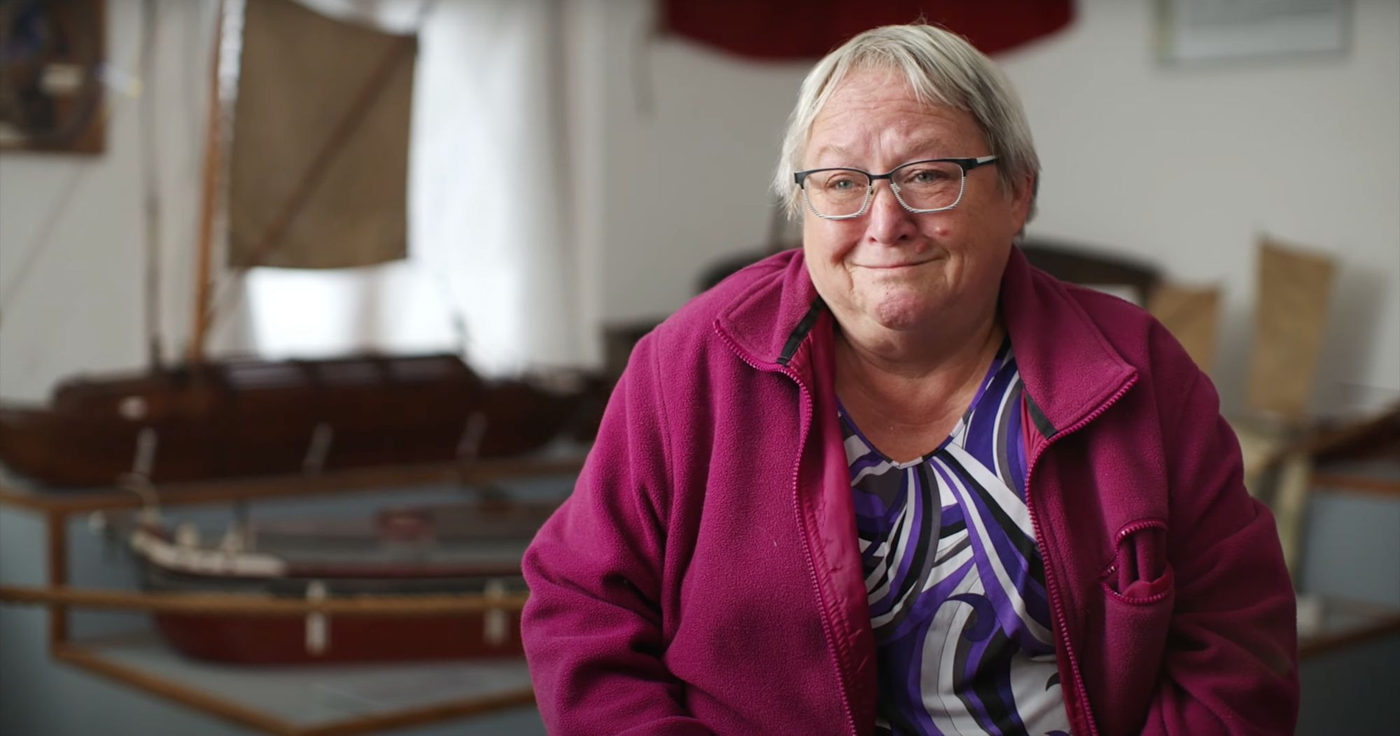 Frau mit Brille lächelt vor unscharfen Schiffsmodellen im Museum