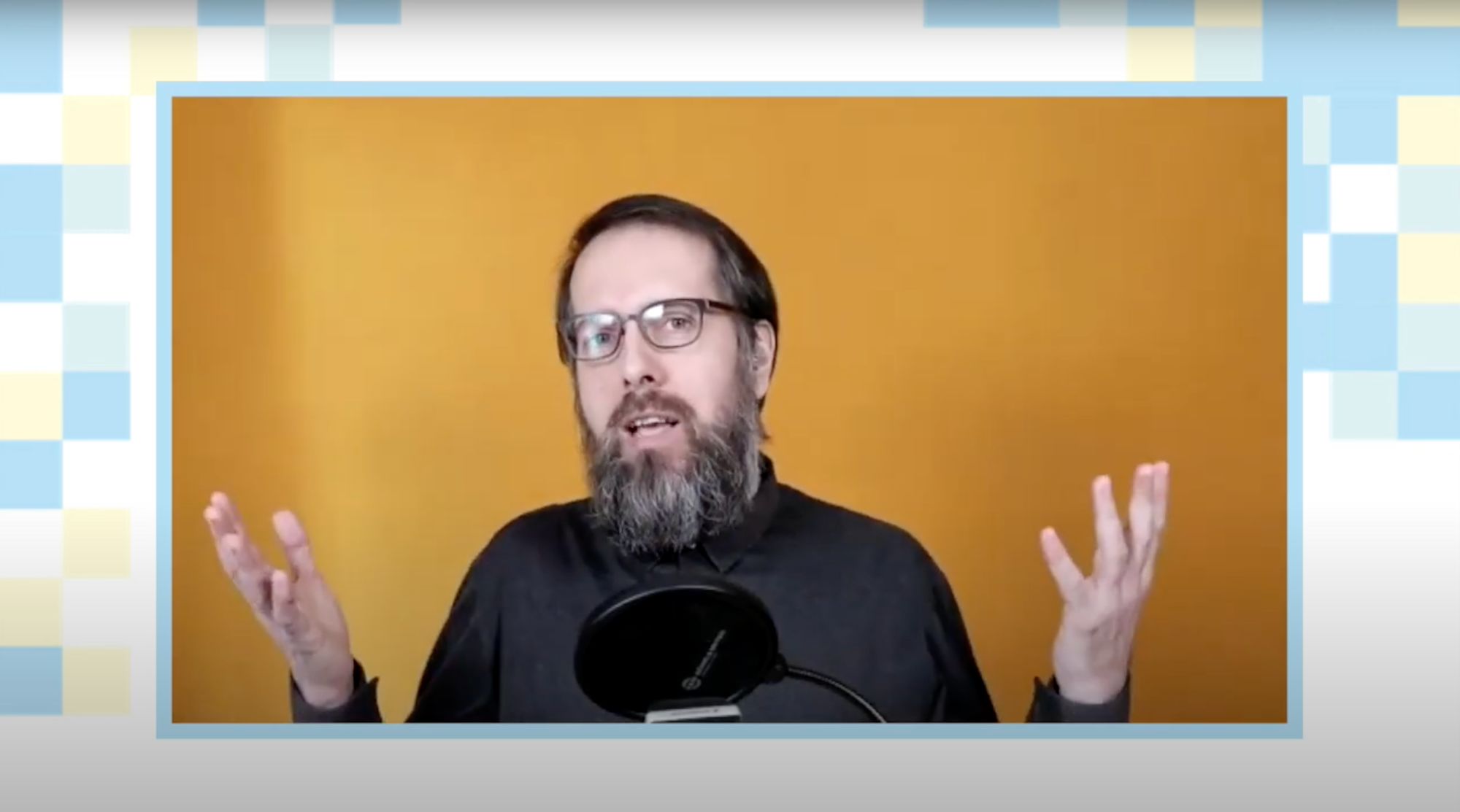 Mann mit Brille und grauem Bart gestikuliert vor orangefarbenem Hintergrund