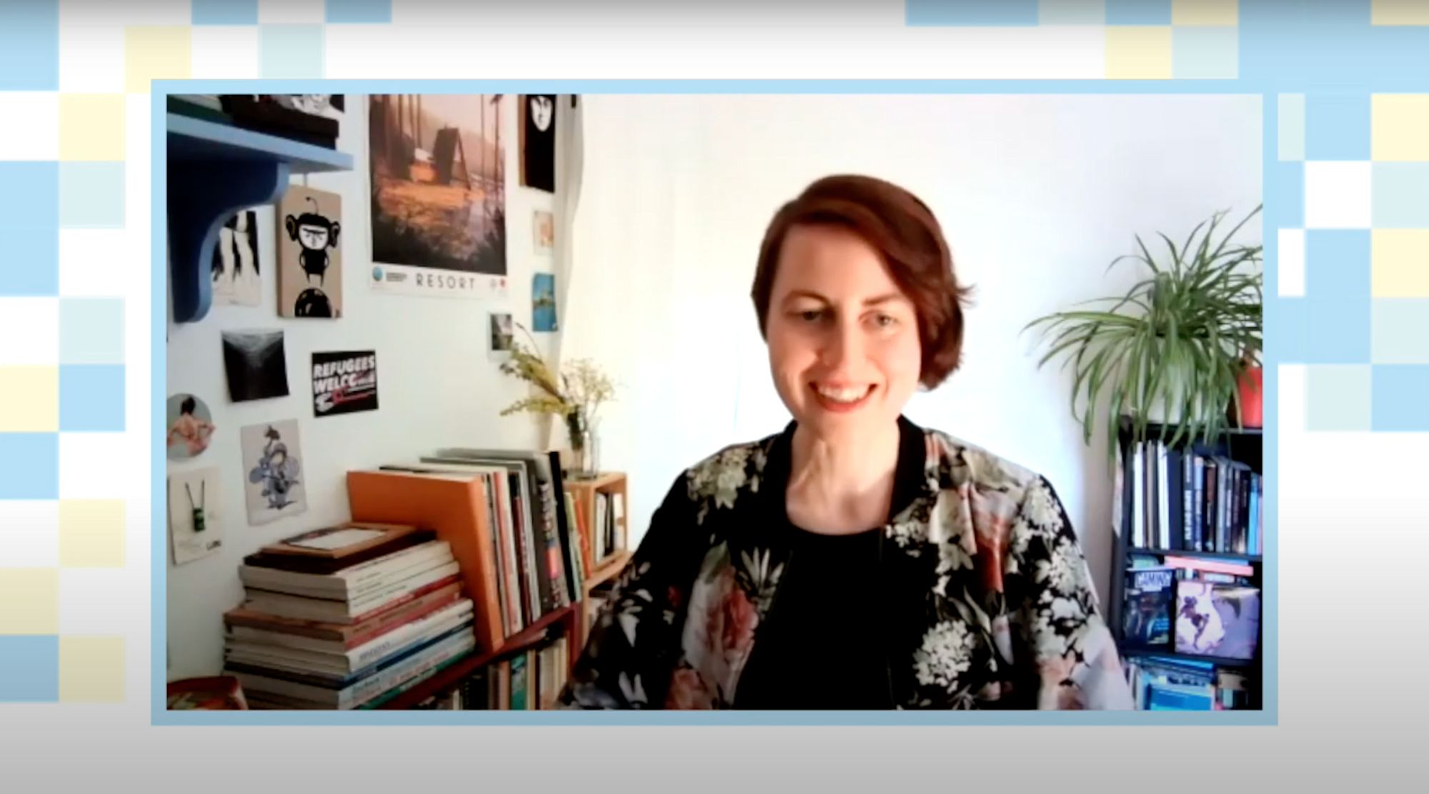 Frau mit kurzen Haaren lächelt vor einem Bücherregal mit Postern im Videocall