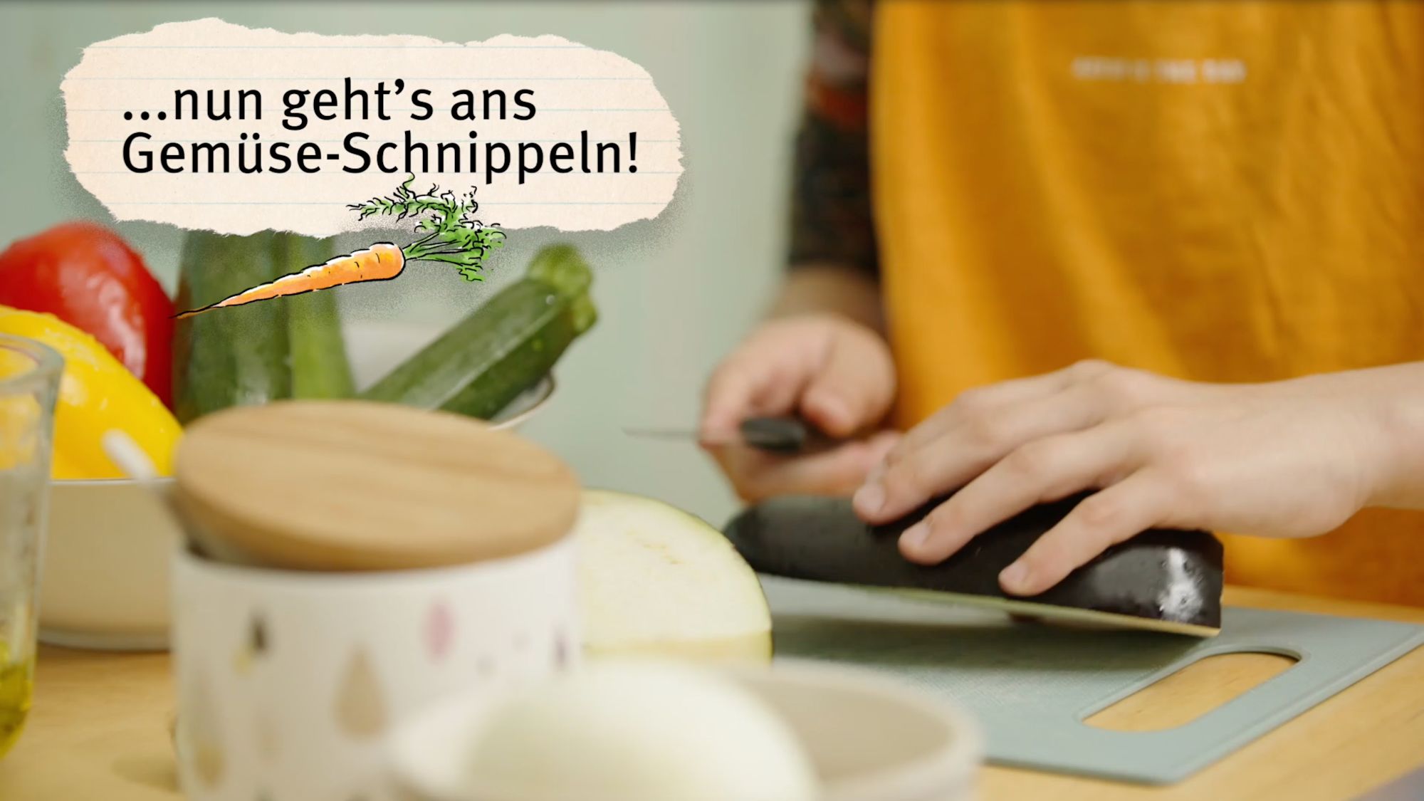 Hände schneiden Zucchini, Bildtext „...nun geht's ans Gemüse-Schnippeln!“ mit gezeichneter Karotte