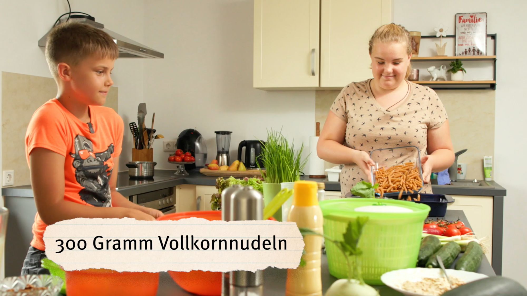 Küchenszene mit Bildtext „300 Gramm Vollkornnudeln“, Junge beobachtet junge Frau beim Kochen