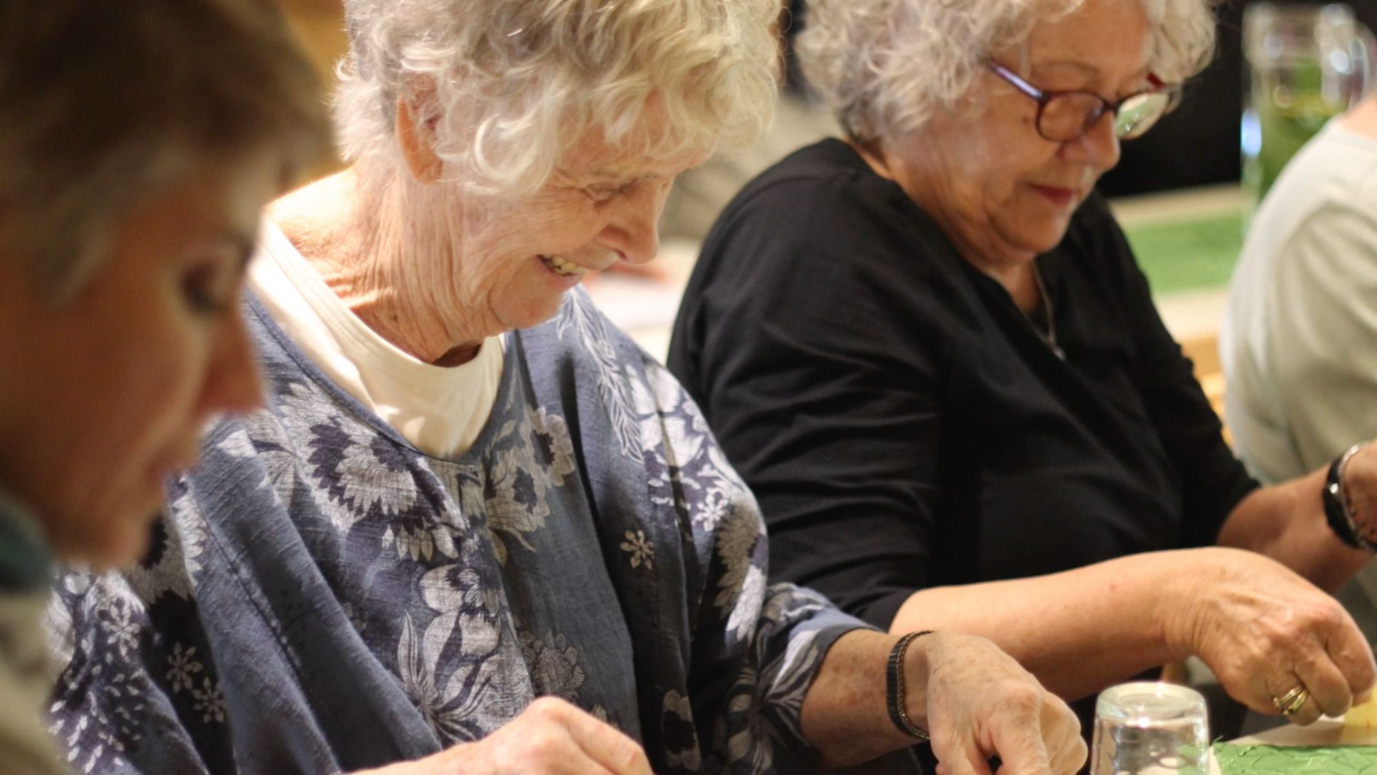Seniorinnen sitzen nebeneinander an einem Tisch und basteln konzentriert