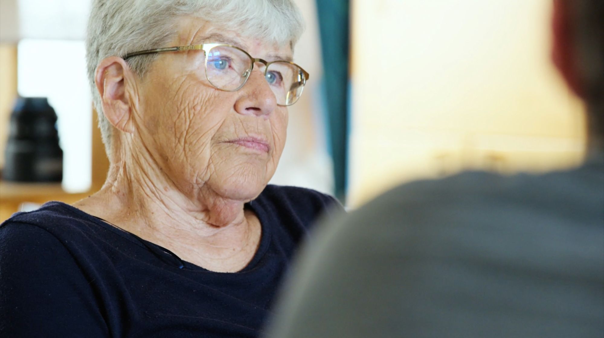 Older woman with glasses looks attentively at the person across from her