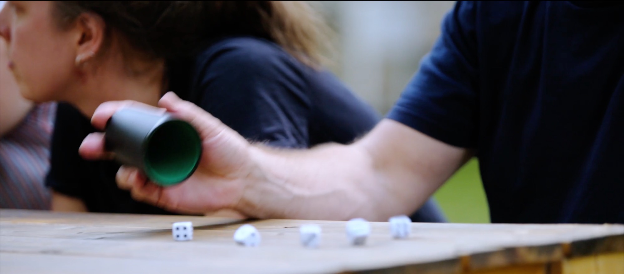 Close-up of a dice cup, with dice being thrown onto an outdoor wooden table