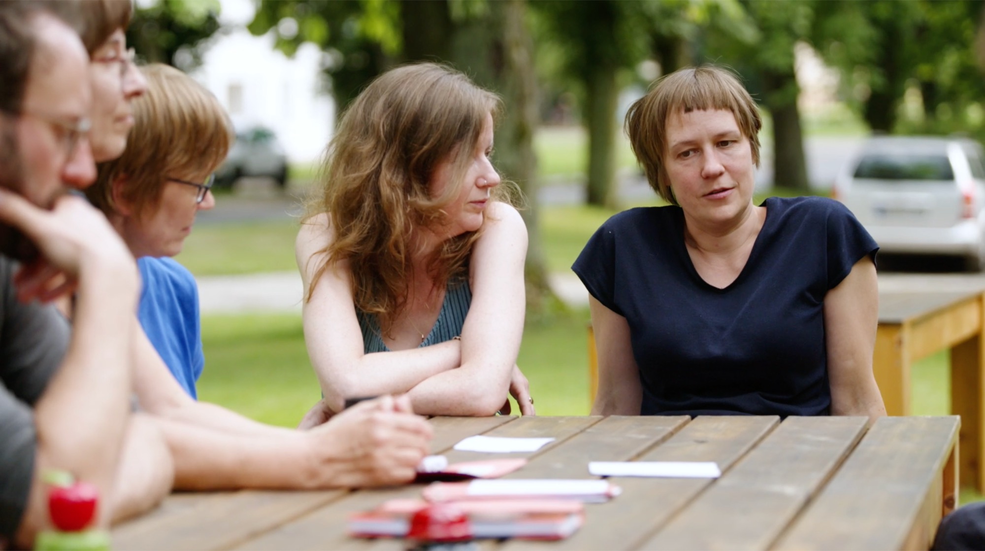 Two women talking at an outdoor table, with other participants in the background