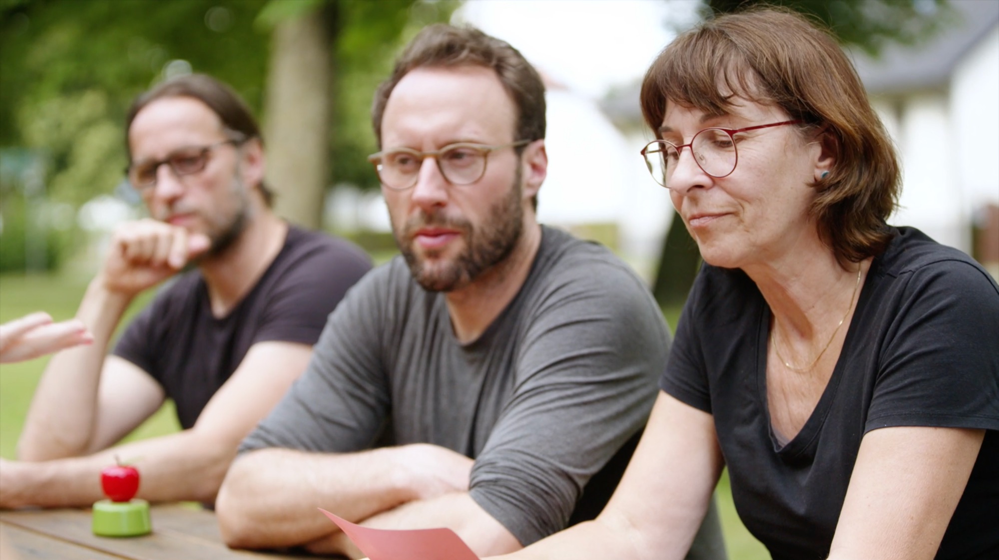 Three people sit talking side by side at an outdoor table
