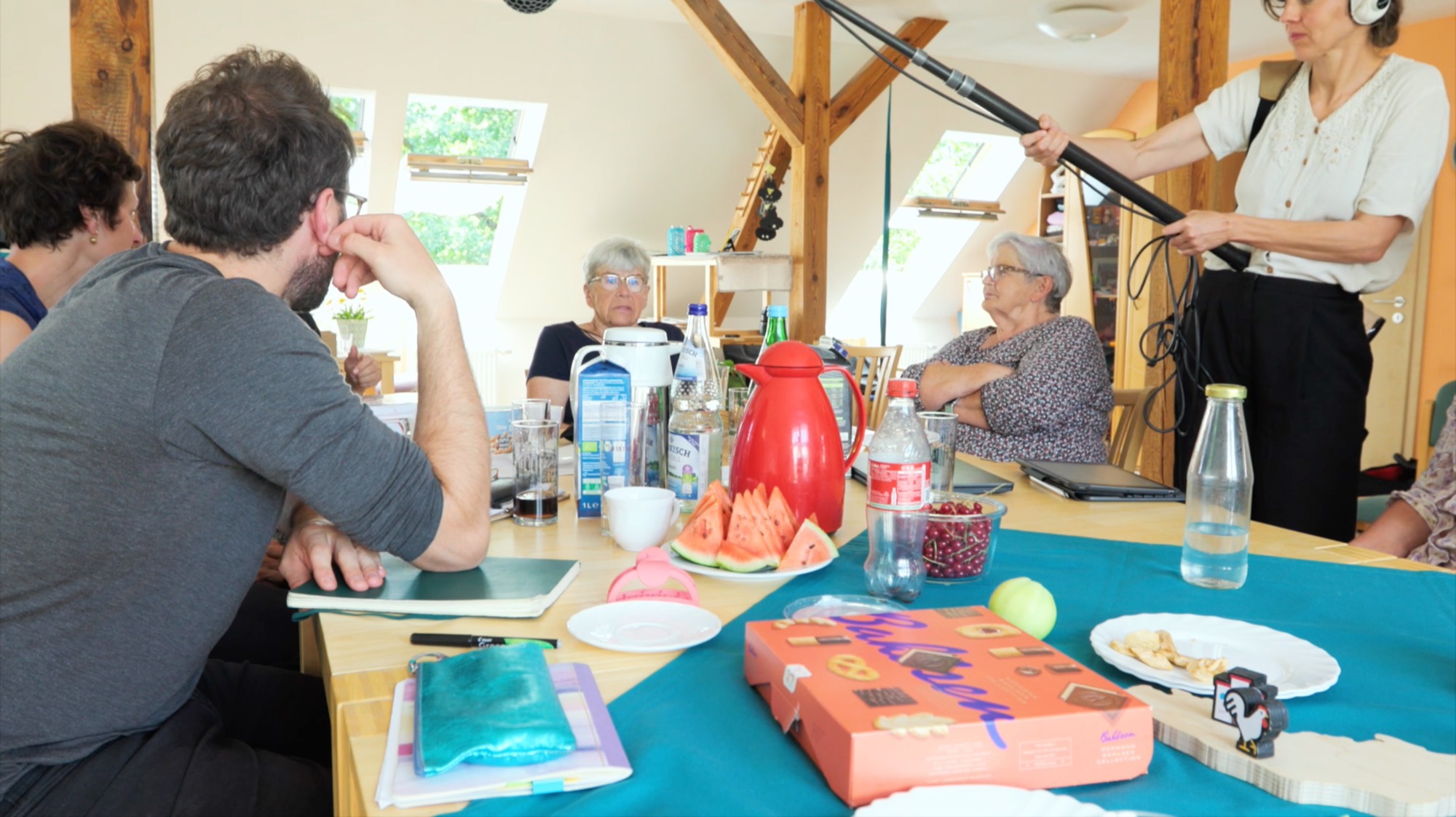 Film crew shooting with a boom microphone in a living space with roof beams
