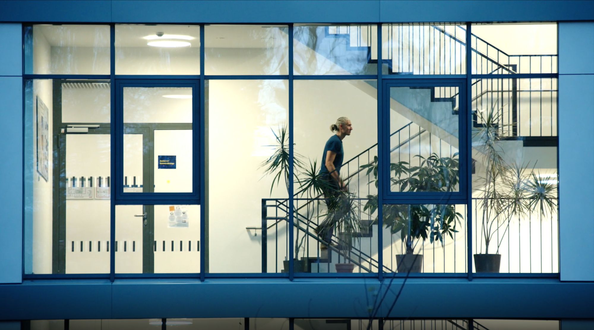Blick durch eine Fensterfront auf ein Treppenhaus, ein Mann geht die Stufen hinauf