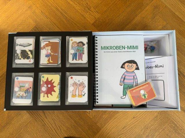Spielschachtel „Mikroben-Mimi“ mit Kartenset und Booklet auf Holztisch