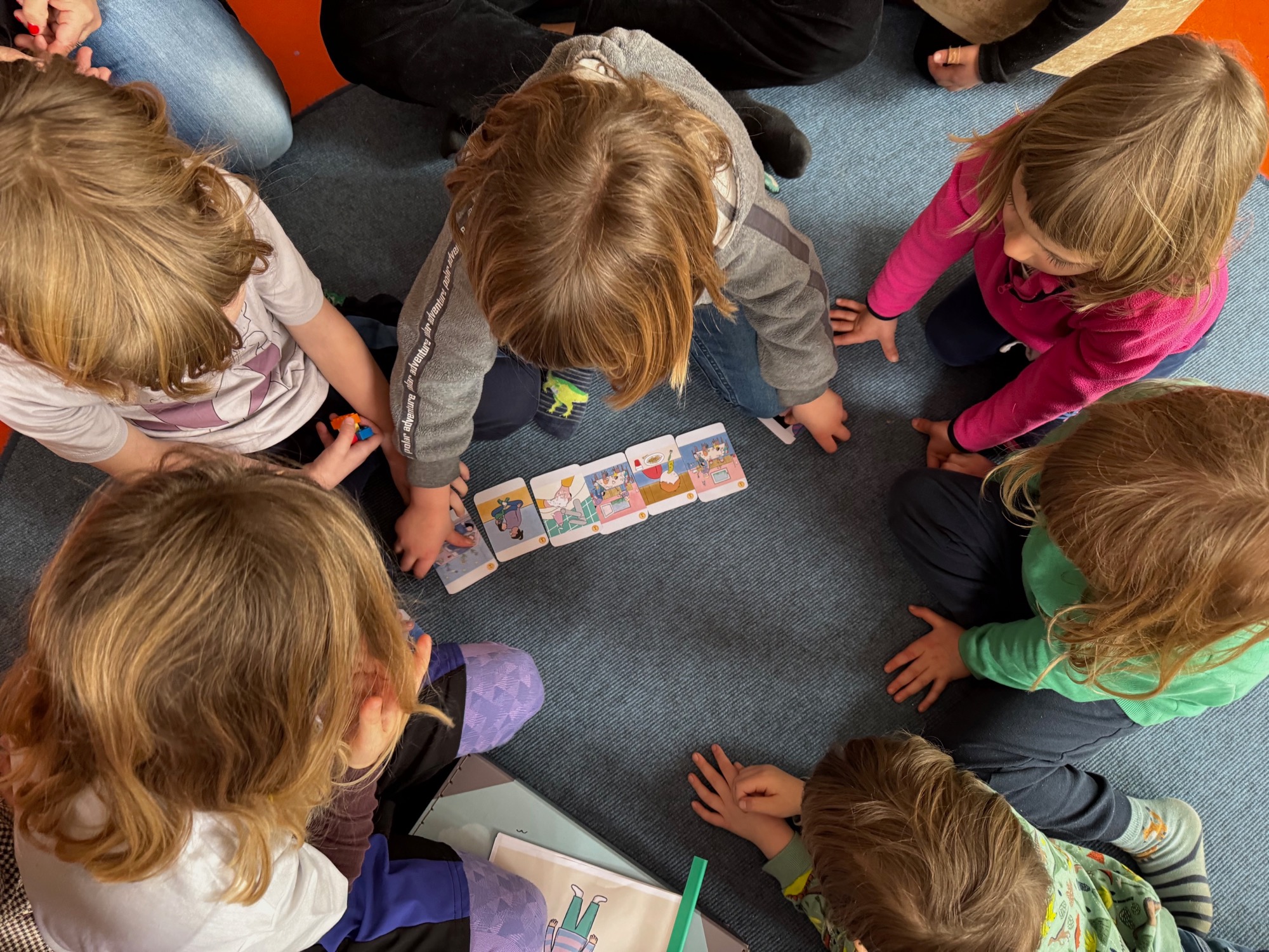 Kinderhände legen von oben fotografiert Bildkarten einer Alltagsgeschichte in eine Reihe