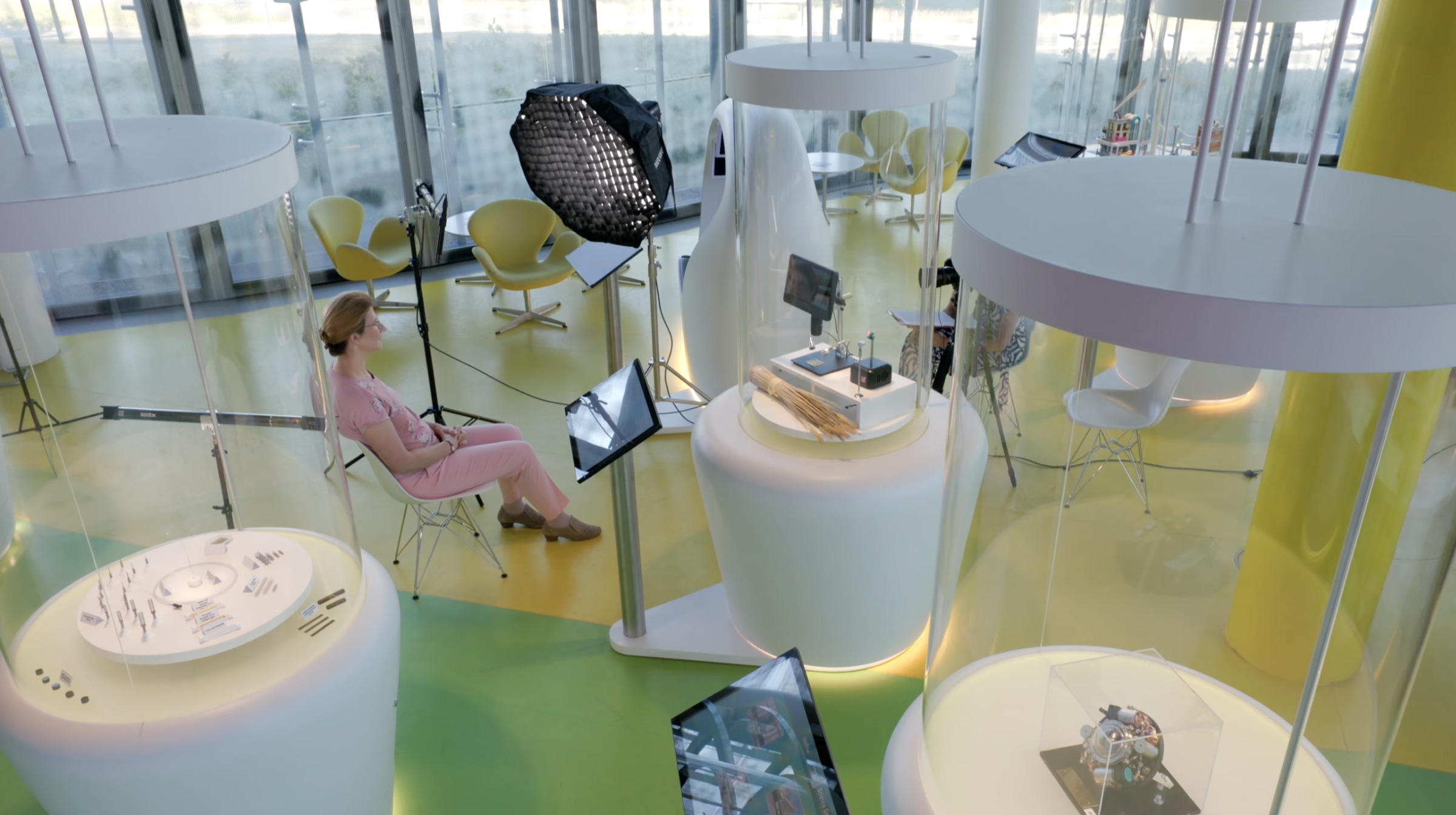 Interviewaufbau in einer Ausstellungshalle – eine Professorin sitzt zwischen gläsernen Vitrinen vor Kamera und Filmlicht