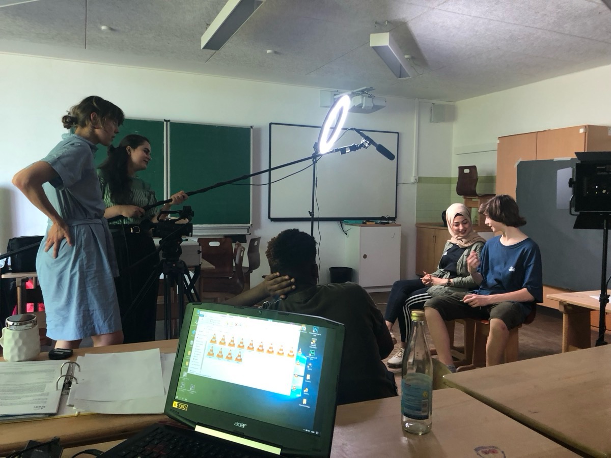 Young people being filmed in a classroom with camera, light and microphone