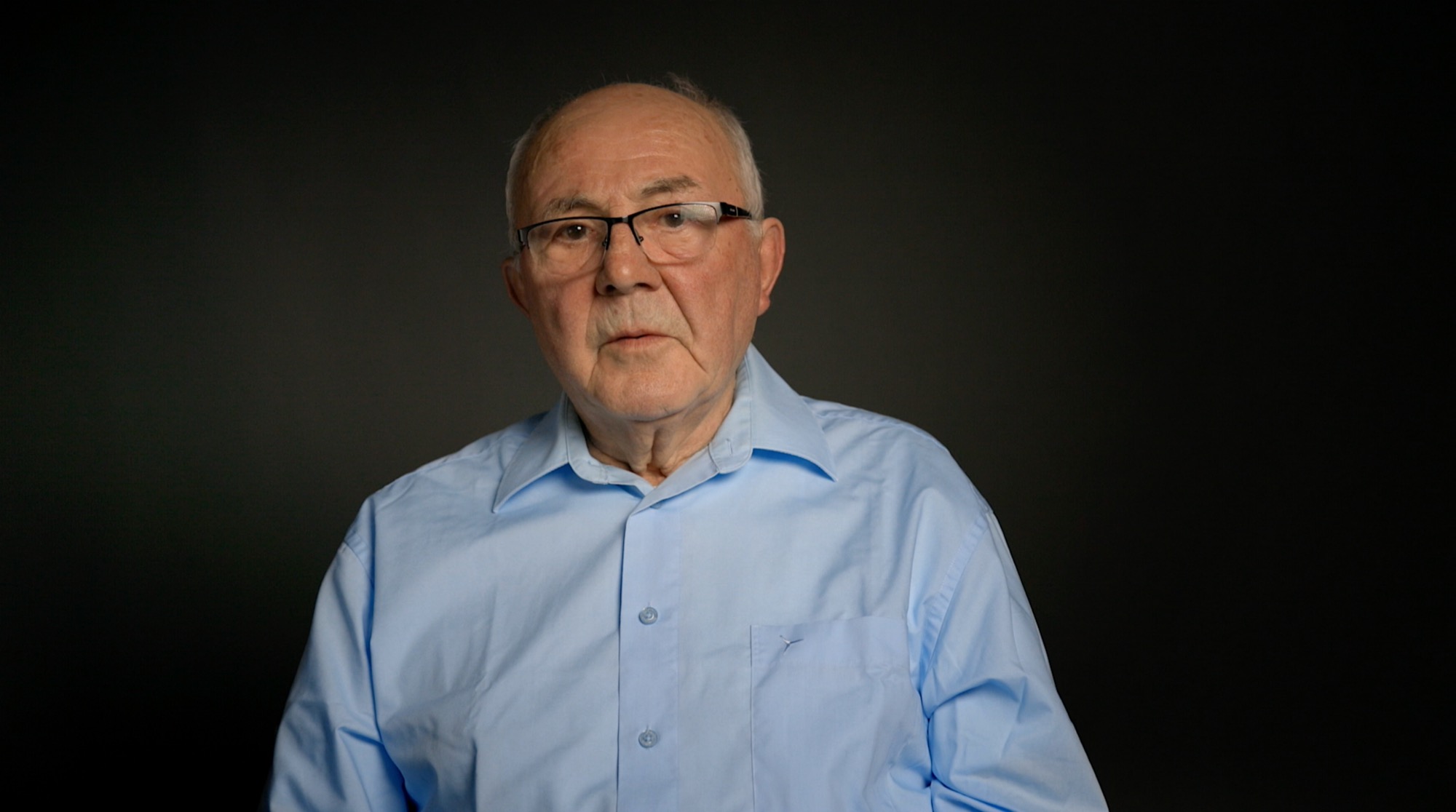 Portrait of an older man in an interview setting against a dark background