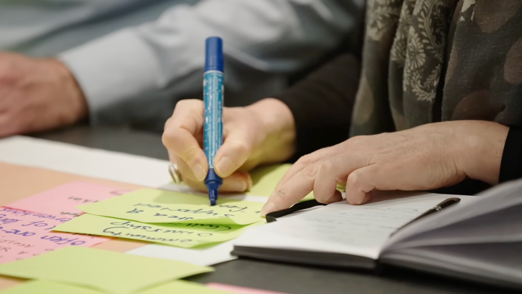 Hands writing on colourful sticky notes beside an open notebook